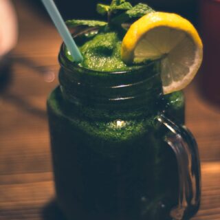 close up photography of clear glass mason jar mug with green juice and sliced citrus toppings
