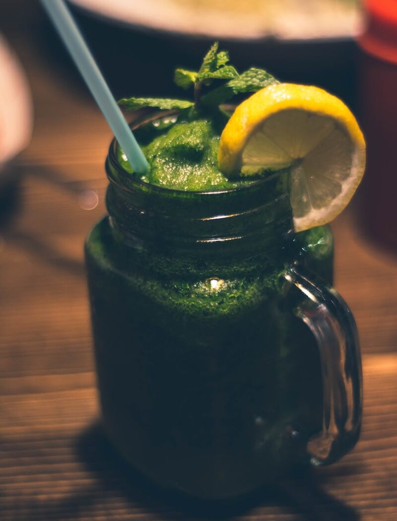 close up photography of clear glass mason jar mug with green juice and sliced citrus toppings